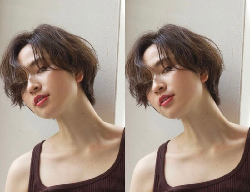 Người với tóc ngắn, mặc áo hai dây màu tối, đứng dựa vào tường, ánh sáng chiếu từ bên trái.
