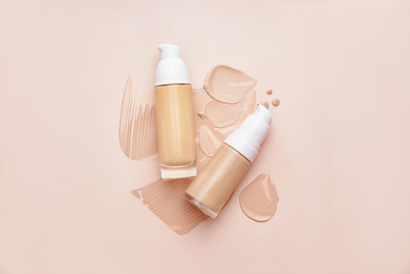 Hai chai kem nền với nắp trắng, đặt trên nền màu be, xung quanh có các vệt kem tán đều.