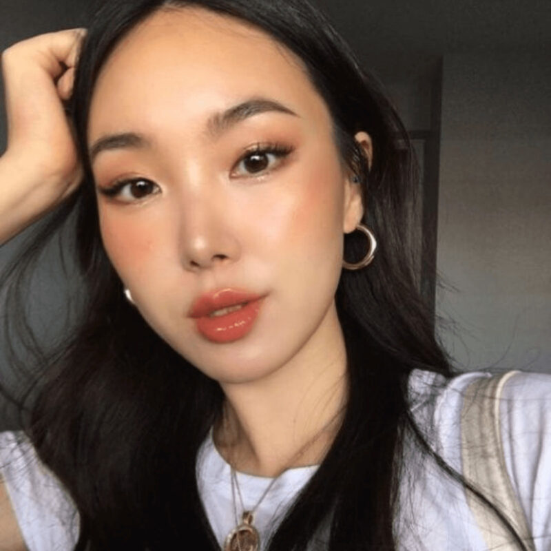 Người phụ nữ với đôi bông tai tròn và áo trắng, tóc đen dài, chụp cận cảnh trong ánh sáng tự nhiên.