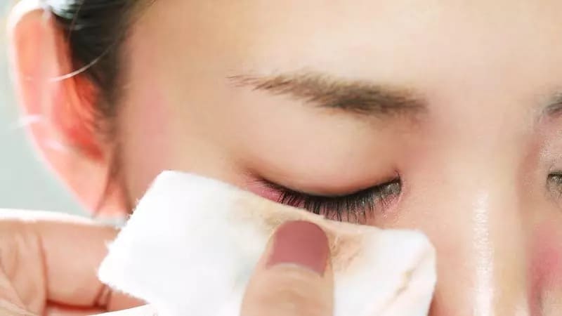 Người đang dùng bông tẩy trang lau mắt để loại bỏ lớp trang điểm.