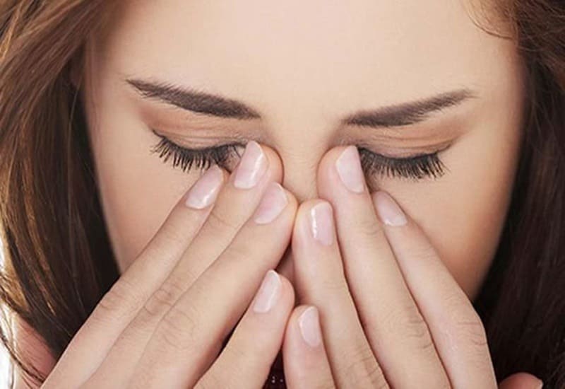 Người đang nhắm mắt, dùng tay xoa nhẹ vùng mũi và mắt, thể hiện sự mệt mỏi hoặc căng thẳng.