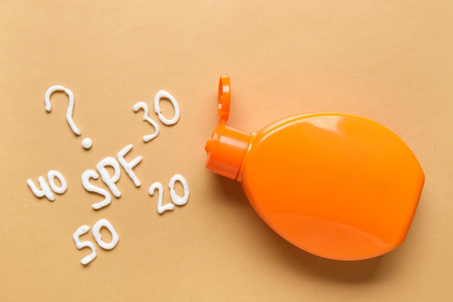 Chai kem chống nắng màu cam, với chữ SPF và số 20, 30, 40, 50 viết bằng kem trên nền màu cam nhạt.