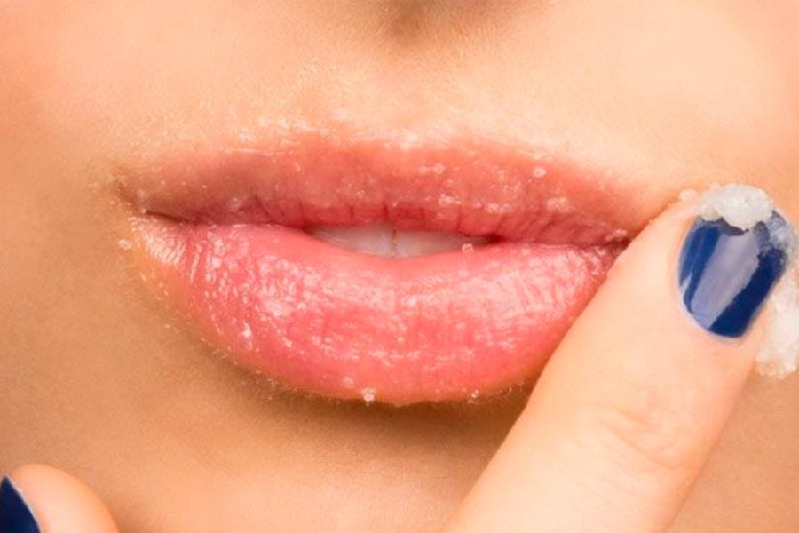 Người dùng thoa hỗn hợp tẩy tế bào chết lên môi, với tay có móng sơn màu xanh đậm.