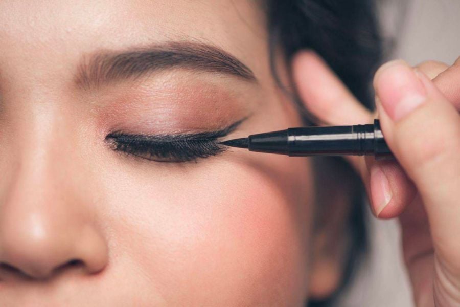 Người đang kẻ mắt bằng bút kẻ mắt nước màu đen, tập trung vào vùng mắt bên phải.