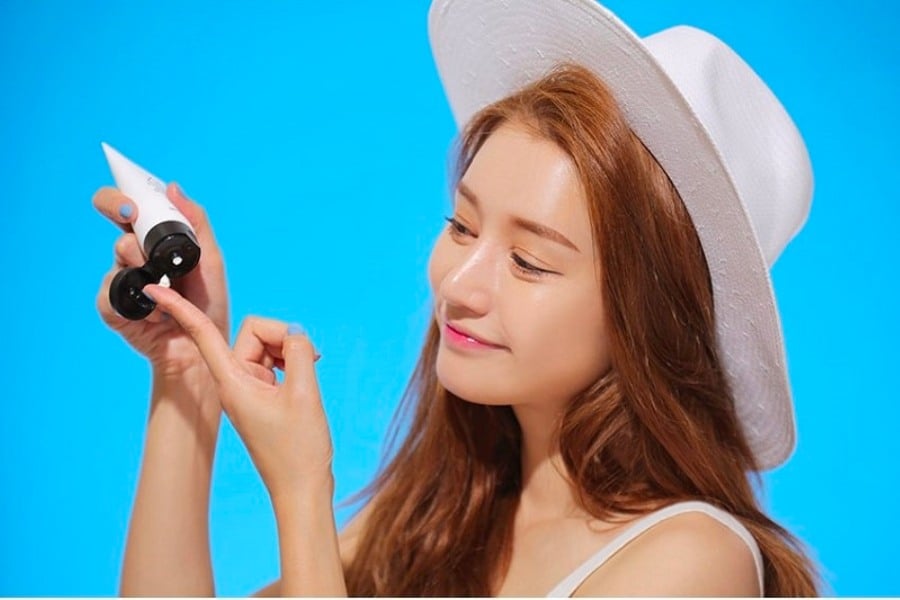 Người đội mũ trắng đang lấy kem từ ống, nền xanh dương.