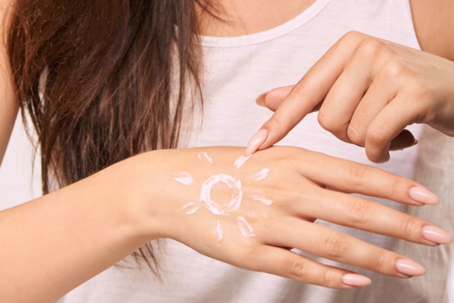 Người đang thoa kem chống nắng lên tay, kem được vẽ thành hình mặt trời trên mu bàn tay.