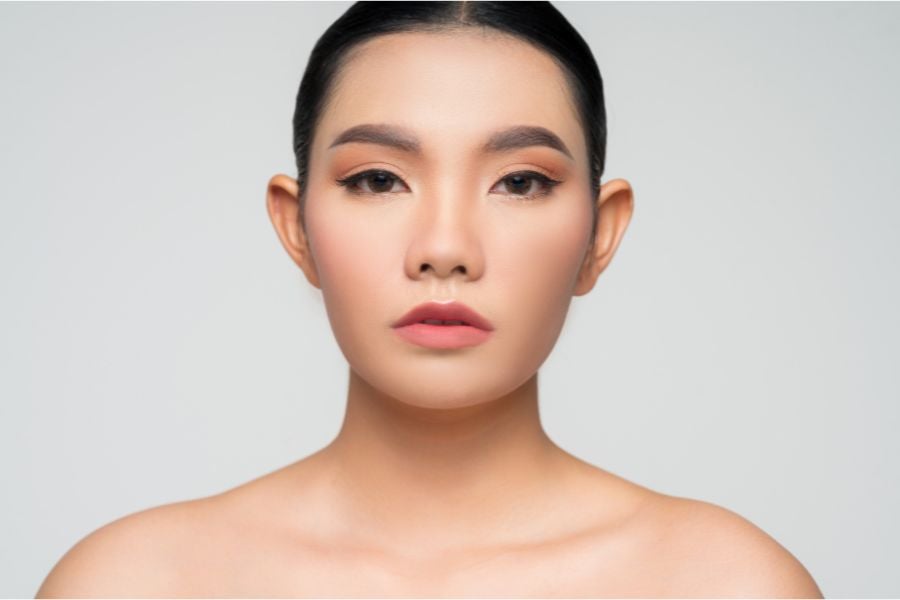 Chân dung một người với làn da mịn, tóc buộc gọn, nhìn thẳng vào máy ảnh trên nền trắng.