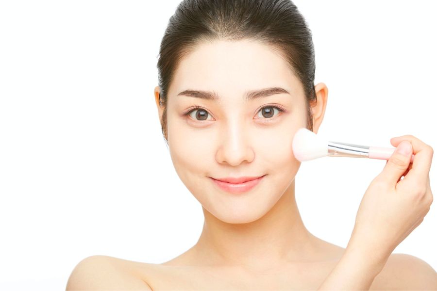 Người cầm cọ trang điểm, mỉm cười nhẹ nhàng, nền trắng.