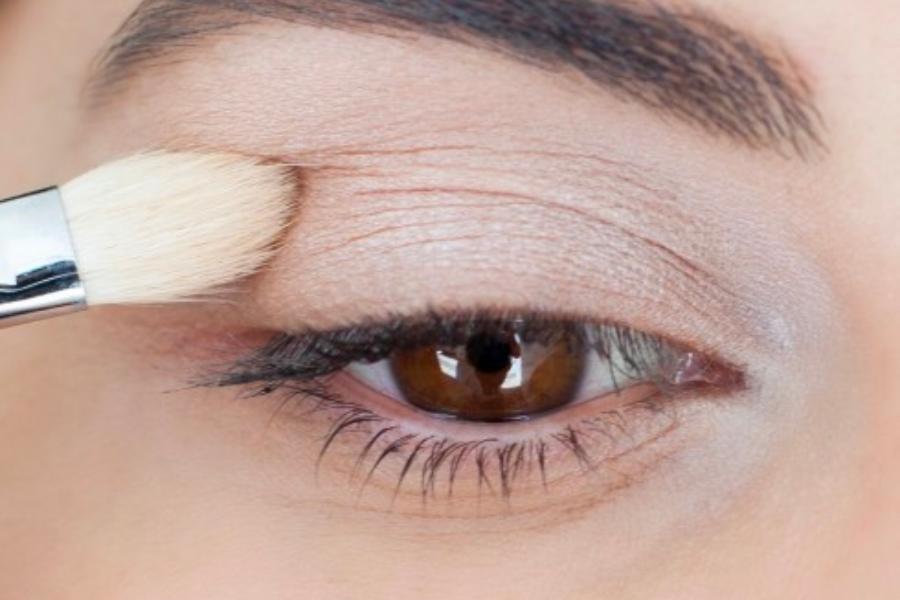 Cận cảnh một cây cọ trang điểm đang thoa phấn mắt lên mí mắt của một người.