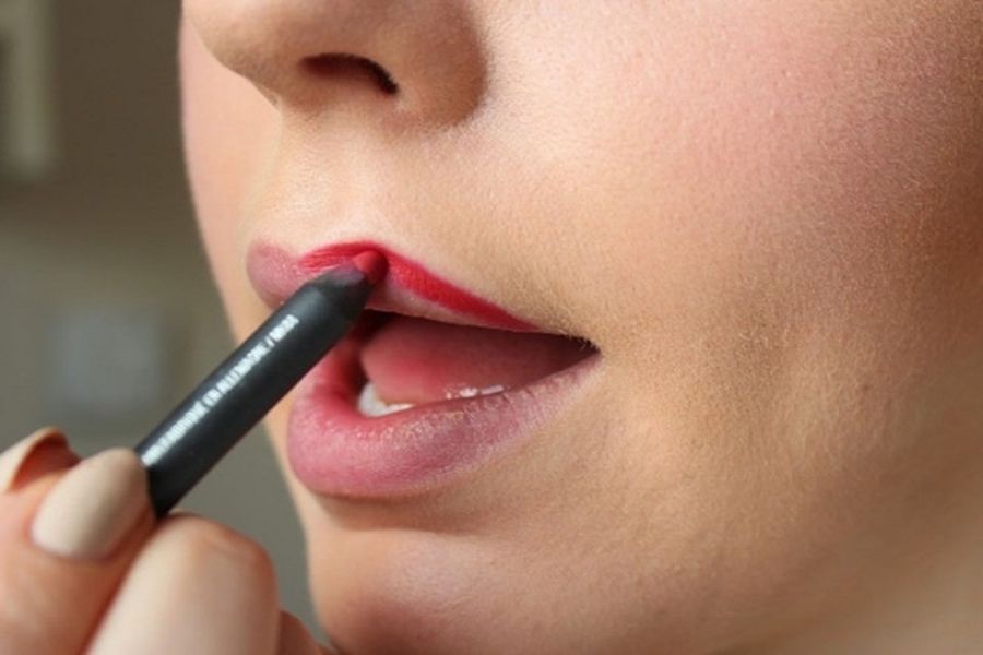 Người đang sử dụng bút kẻ môi màu đỏ để tô viền môi, cận cảnh phần mặt và môi.