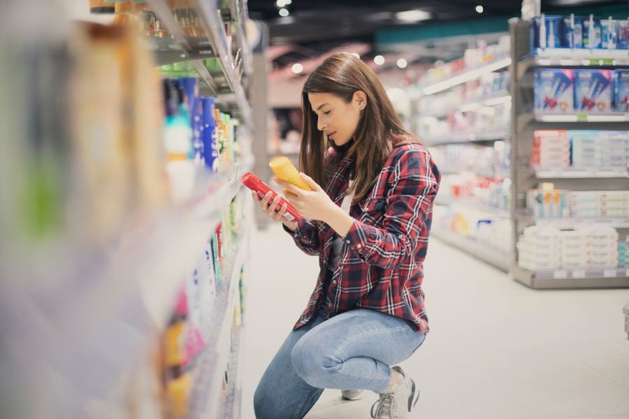 Người phụ nữ mặc áo kẻ caro đang xem xét sản phẩm trong một cửa hàng, cầm hai chai trên tay.
