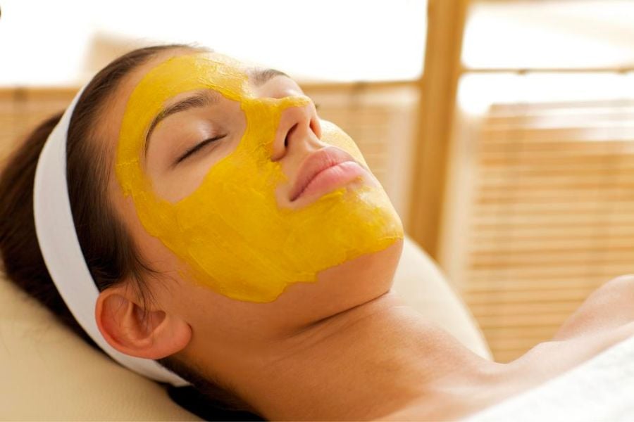 Người nằm thư giãn với mặt nạ dưỡng da màu vàng trên mặt trong không gian spa.