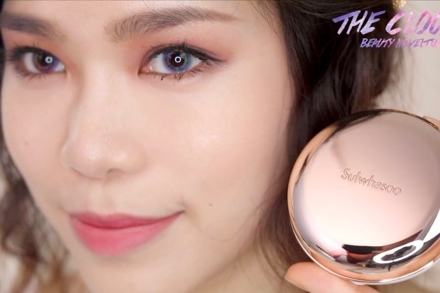 Người cầm hộp phấn nền màu vàng hồng có chữ "Sulwhasoo", khuôn mặt trang điểm nhẹ nhàng.