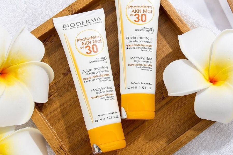 Hai tuýp kem chống nắng Bioderma SPF 30 đặt trên khay gỗ, kèm hoa trắng trang trí.