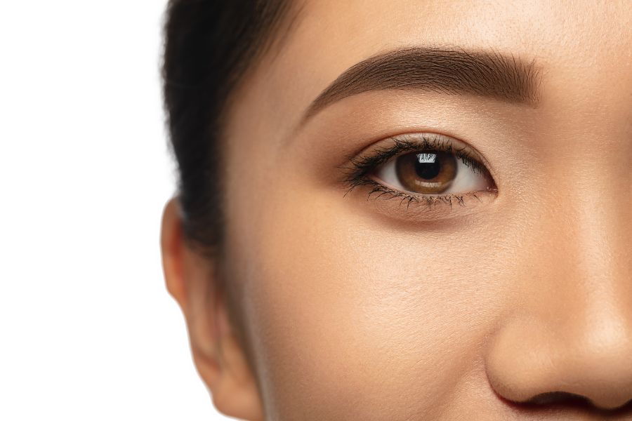Cận cảnh một bên mắt và chân mày của người, nền trắng.