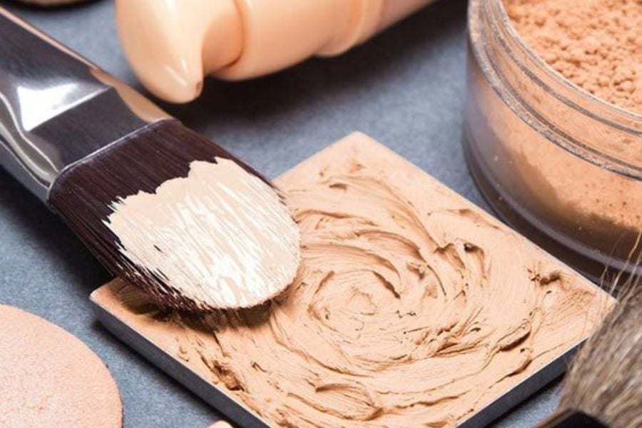 Cọ trang điểm với kem nền và phấn phủ trên nền xám.