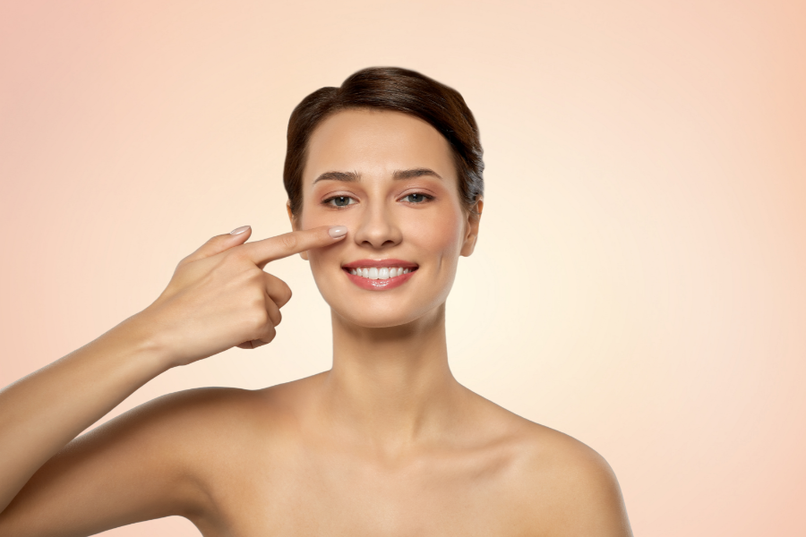 Người phụ nữ cười, dùng ngón tay chỉ vào má, nền màu hồng nhạt.