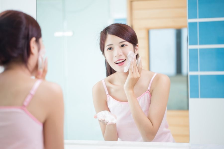Người phụ nữ đang rửa mặt với bọt xà phòng trước gương trong phòng tắm.