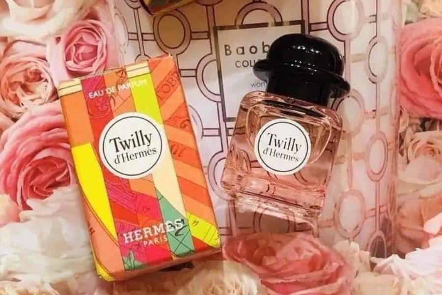 Hộp và chai nước hoa trên nền hoa hồng, thiết kế màu sắc nổi bật và sang trọng.