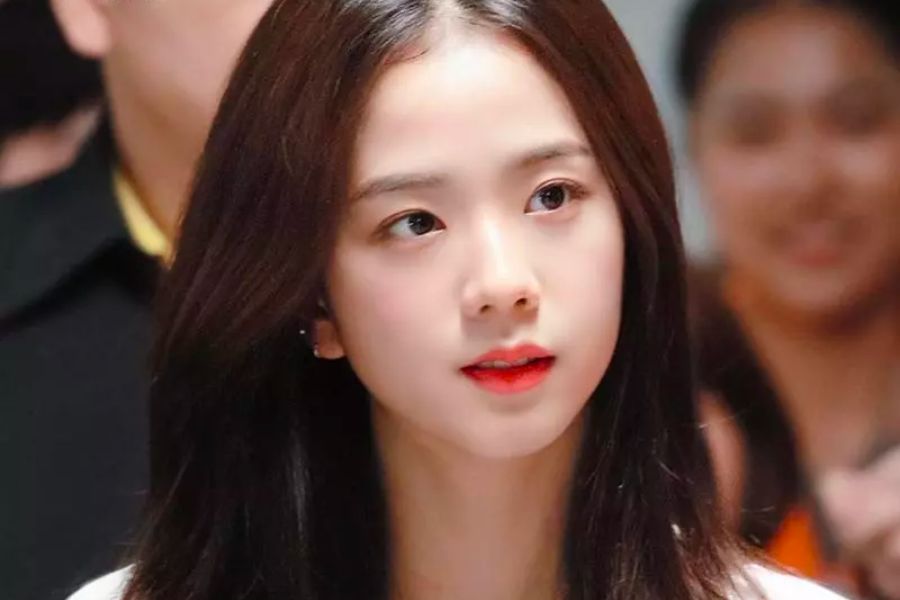 Người phụ nữ tóc đen dài, môi đỏ, ánh mắt nhìn xa xăm trong một không gian đông người.