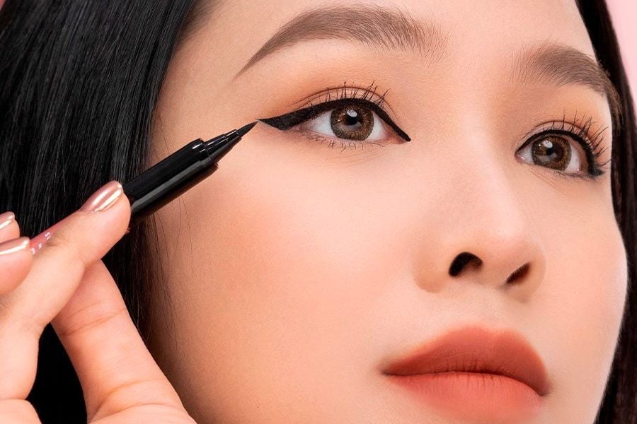 Người đang kẻ mắt với bút kẻ mắt màu đen, tạo đường viền sắc nét trên mí mắt.