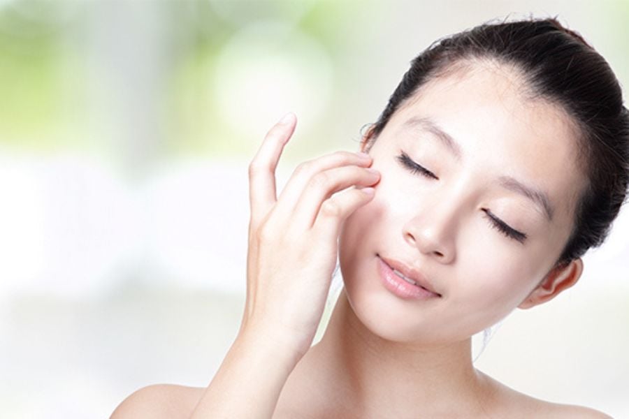 Người phụ nữ chạm nhẹ vào má, mắt nhắm, thể hiện sự thư giãn và chăm sóc da mặt.