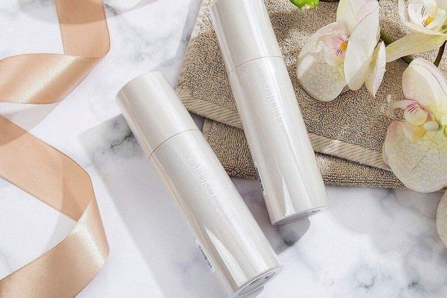Hai chai mỹ phẩm màu trắng trên nền đá cẩm thạch, bên cạnh hoa lan và dải ruy băng màu be.