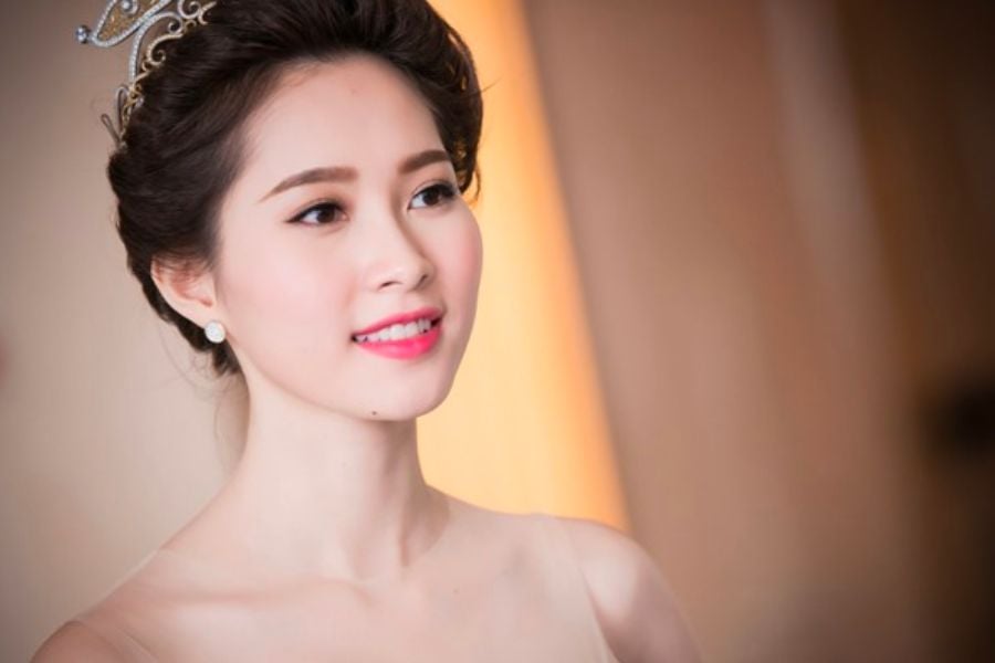 Người phụ nữ đeo vương miện và trang sức, mặc váy, nhìn về phía trước với phông nền mờ.