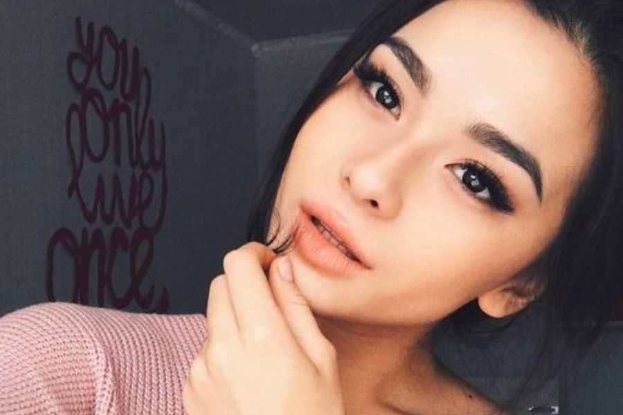 Một người chụp ảnh tự sướng, mặc áo hồng, nền có dòng chữ trang trí trên tường.
