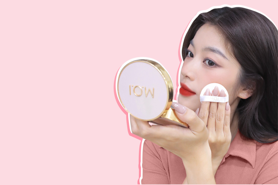 Người cầm hộp phấn trang điểm và đang dặm phấn lên mặt trên nền hồng.