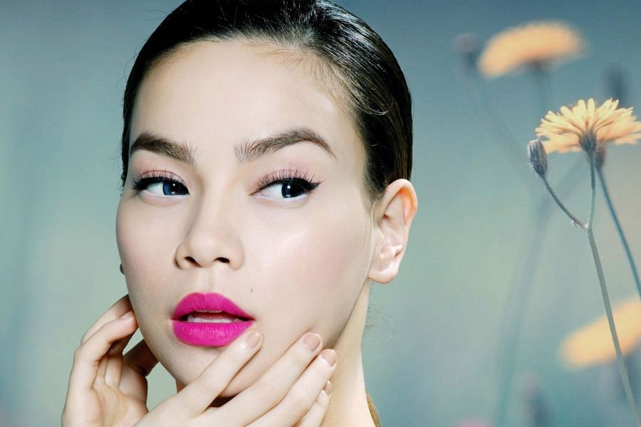 Người phụ nữ trang điểm đậm, môi hồng, với nền hoa mờ phía sau.