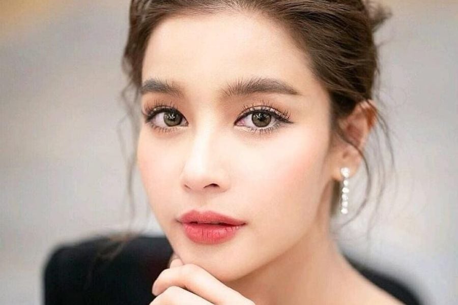 Người phụ nữ với mái tóc búi gọn, đeo hoa tai, nhìn thẳng vào máy ảnh.