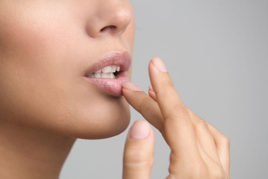 Người đang chạm nhẹ vào môi của mình bằng ngón tay, thể hiện cử chỉ chăm sóc da môi.