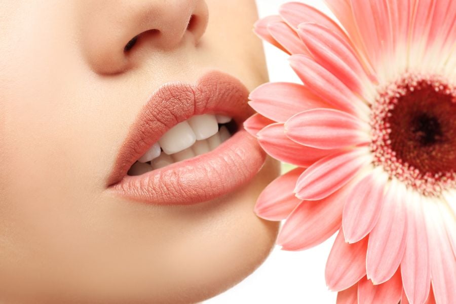 Đôi môi gần một đóa hoa cúc màu hồng nhạt, tạo nên sự hài hòa và tinh tế giữa thiên nhiên và con người.