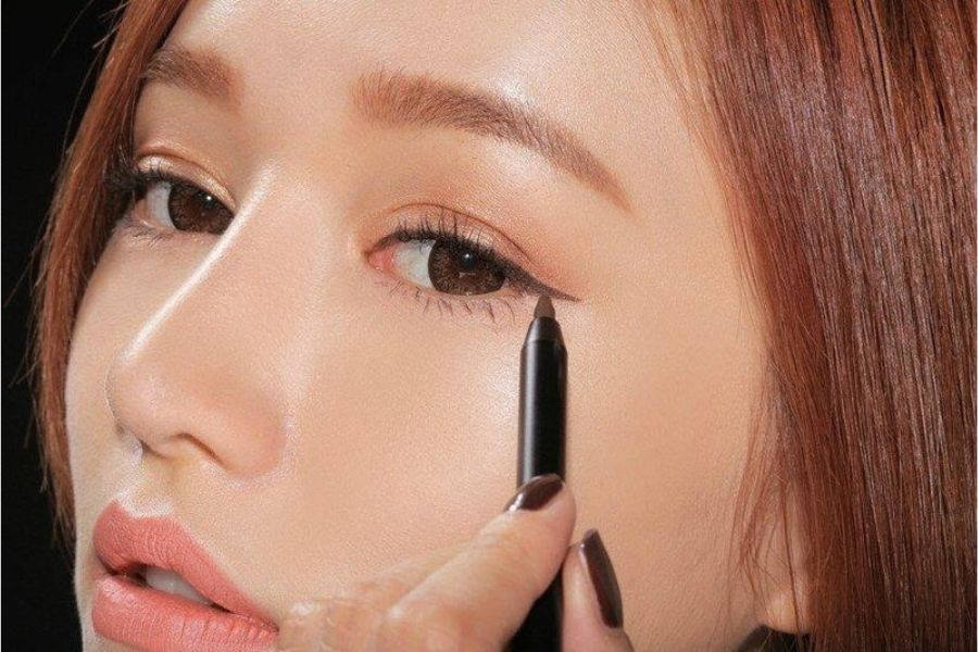 Người đang dùng bút kẻ mắt đen để vẽ eyeliner, tạo điểm nhấn cho đôi mắt.