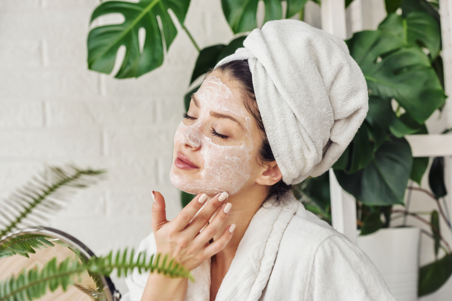 Người phụ nữ đắp mặt nạ dưỡng da, quấn khăn trên đầu, thư giãn trong không gian với cây xanh xung quanh.