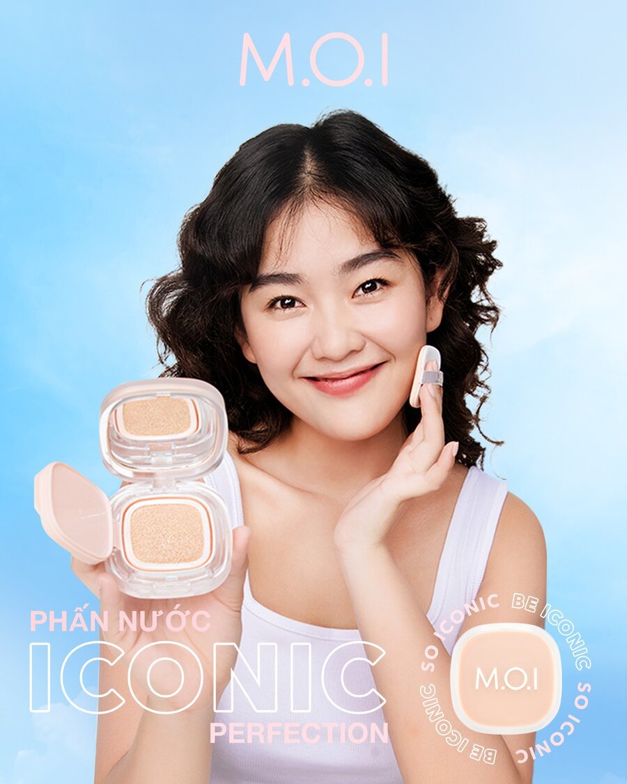 Người phụ nữ dùng phấn nước, cầm hộp phấn M.O.I, nền trời xanh.