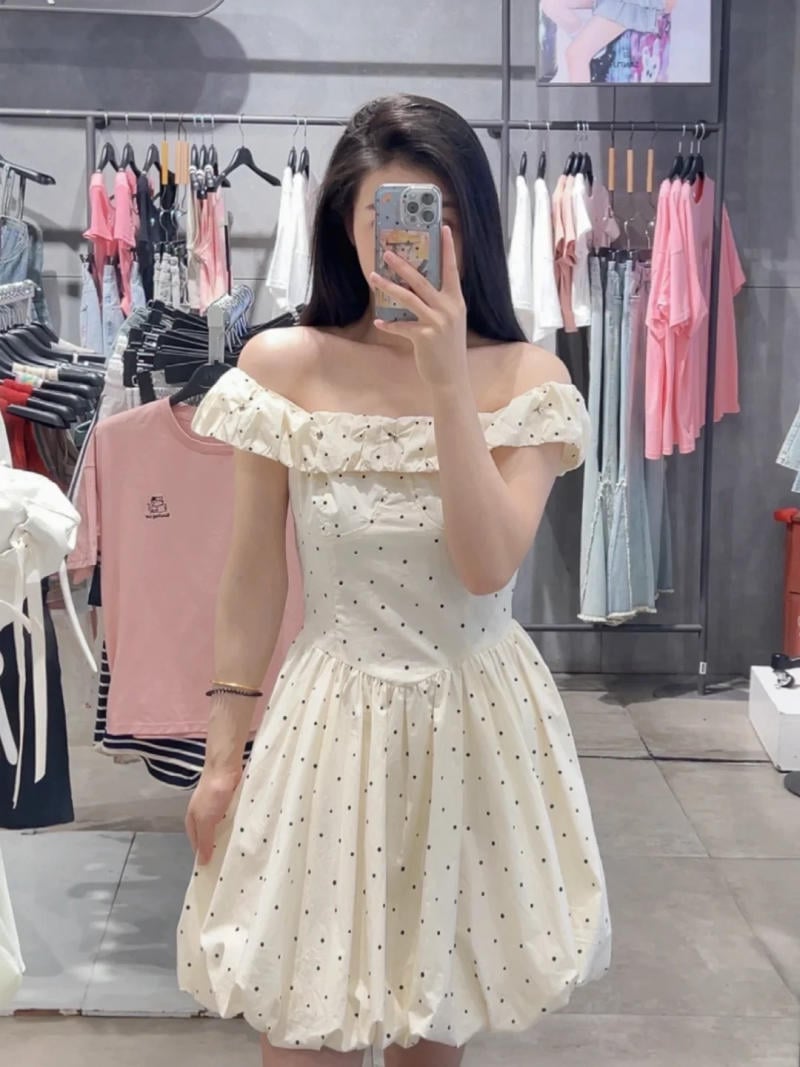 Người phụ nữ mặc váy trắng chấm bi, chụp ảnh tự sướng trong một cửa hàng quần áo.