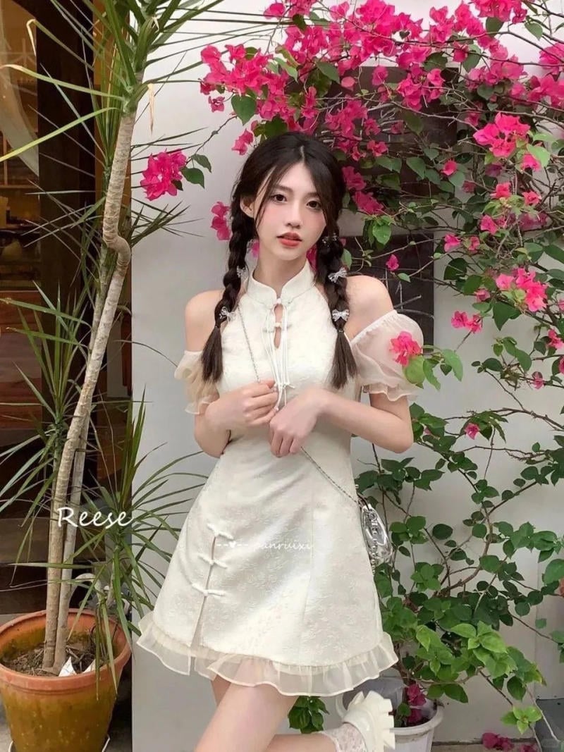 Người mặc váy trắng đứng trước cây hoa giấy hồng, tạo dáng chụp ảnh ngoài trời.