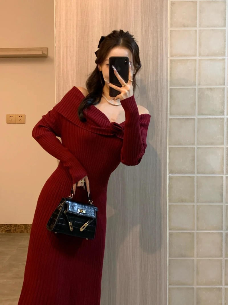 Người mặc váy đỏ, chụp ảnh tự sướng trước gương, tay cầm điện thoại và túi xách đen.