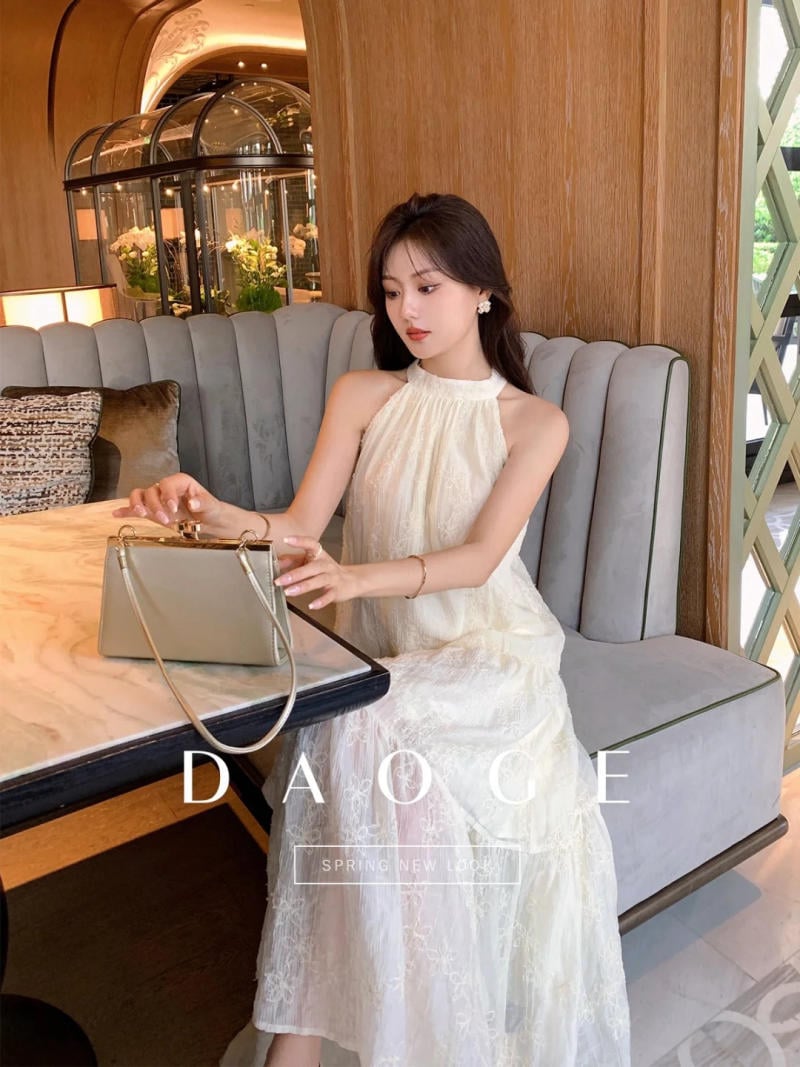 Người phụ nữ mặc váy trắng ngồi trên ghế sofa, tay cầm túi xách, trong không gian nội thất sang trọng.