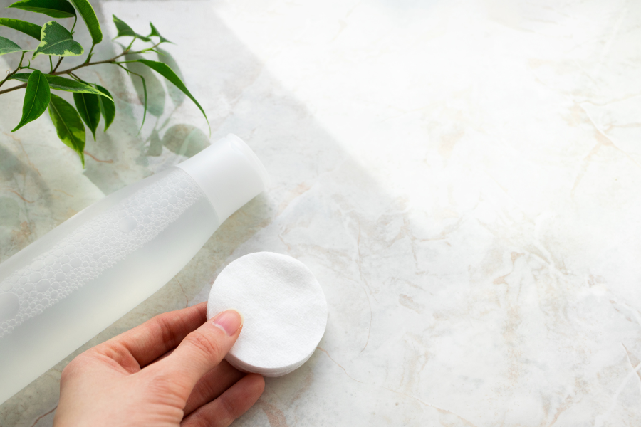 Chai nước và bông tẩy trang trên mặt bàn đá cẩm thạch, cạnh nhánh cây xanh.