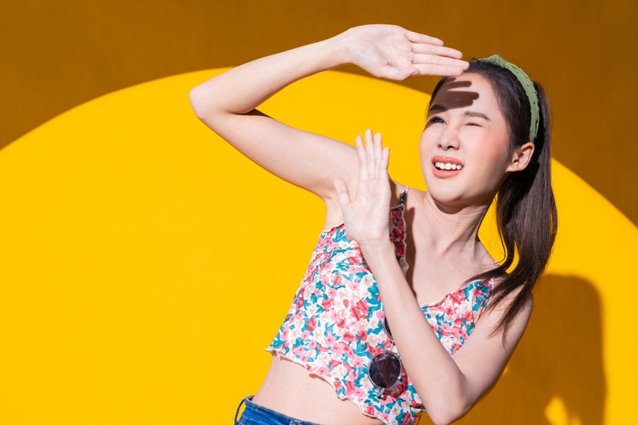 Người phụ nữ mặc áo hoa, giơ tay che nắng, đứng trước nền vàng sáng.