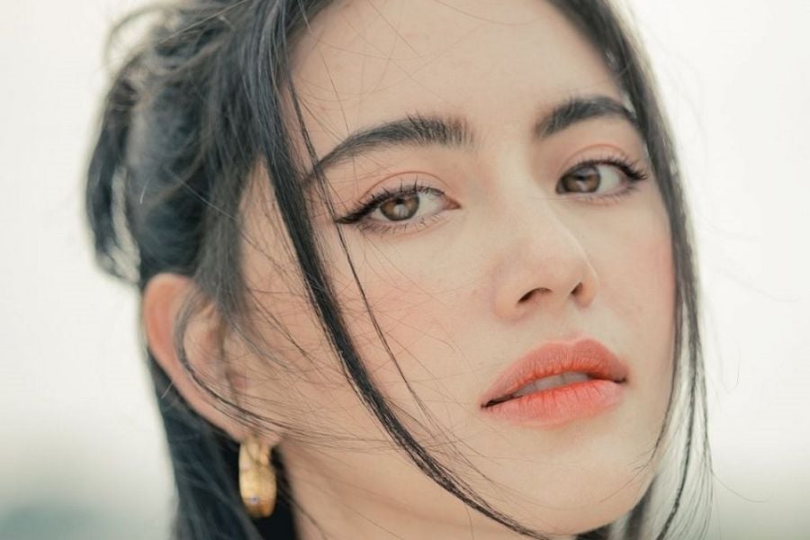 Cận cảnh khuôn mặt người phụ nữ với ánh mắt trực diện, tóc đen và đôi môi son cam.