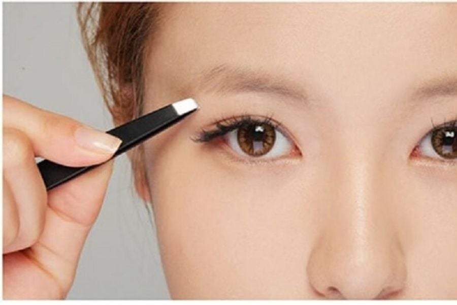 Người dùng cầm nhíp nhổ lông mày, cận cảnh khuôn mặt với đôi mắt và lông mày rõ nét.