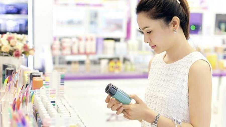Người phụ nữ đang xem sản phẩm trong cửa hàng mỹ phẩm, xung quanh là nhiều chai lọ được sắp xếp ngăn nắp.