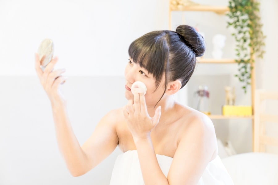 Người phụ nữ đang trang điểm trước gương cầm tay trong phòng sáng sủa.