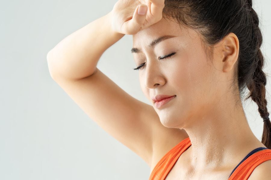 Người phụ nữ mệt mỏi, đặt tay lên trán, mặc áo cam, tóc tết đuôi sam, biểu cảm nhắm mắt thư giãn.