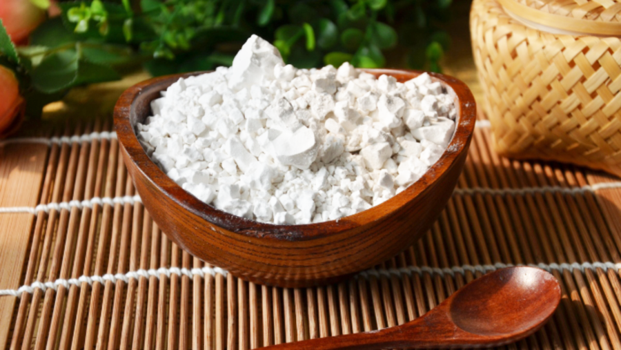 Bát gỗ chứa bột màu trắng, đặt trên tấm trải tre, cạnh một chiếc thìa gỗ và một giỏ đan.