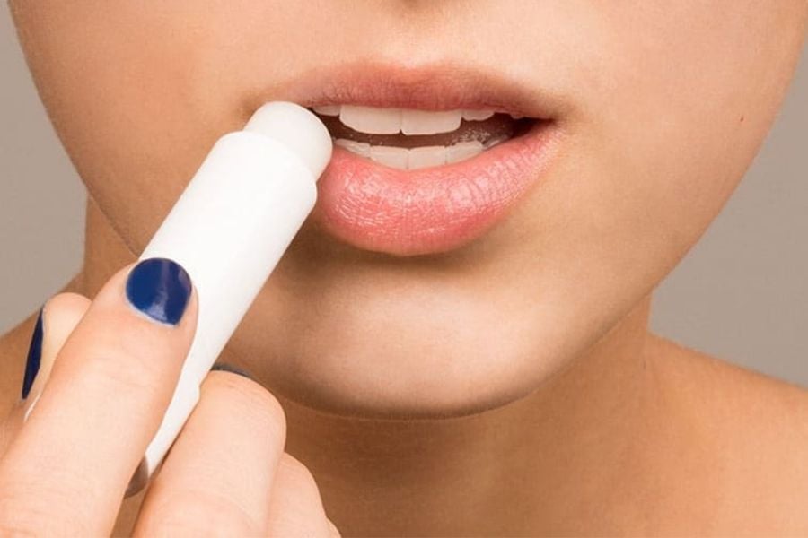 Cận cảnh một người đang thoa son dưỡng lên môi, móng tay sơn màu xanh dương.